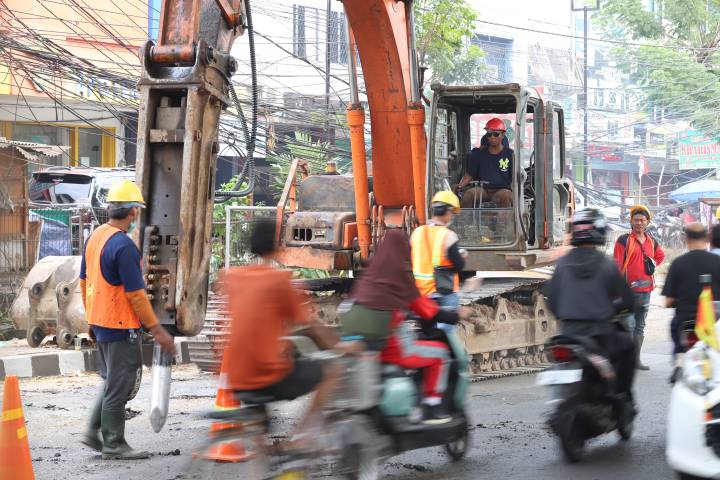 Potret warga lokal dan pengendara motor melintasi pembatas proyek perbaikan di Jalan Raya M. Toha Karawaci yang sedang diekskavasi untuk penguatan struktur beton.